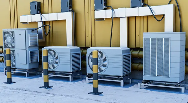 Industrial HVACS and safety bollards along a yellow building wall.