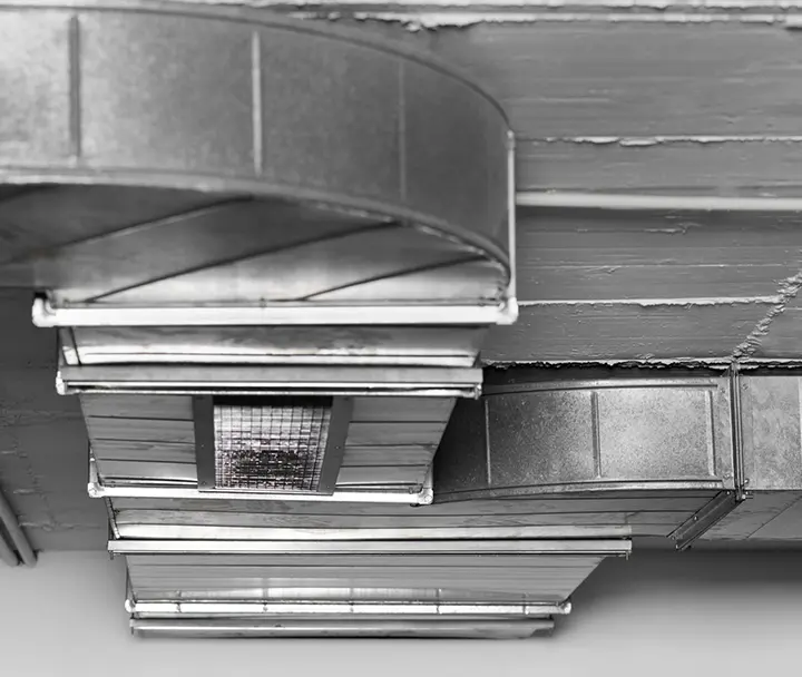 A network of overlapping grey metal HVAC ductwork with a visible internal mesh filter.