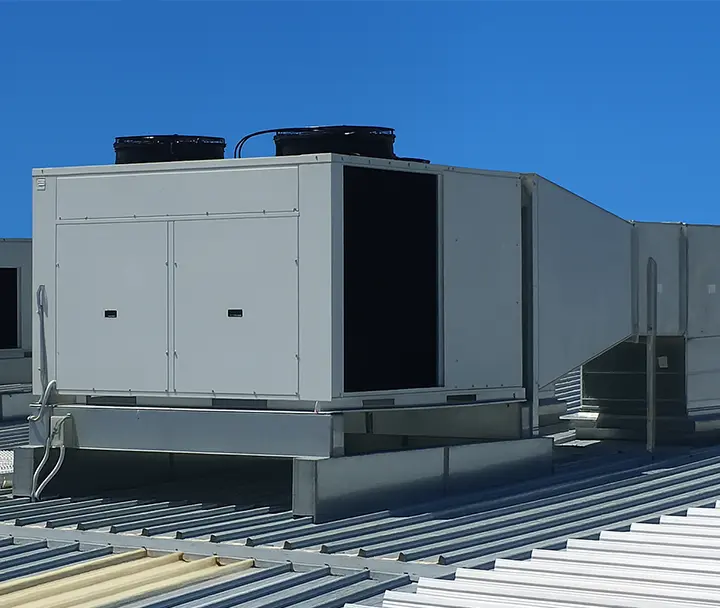 A large white industrial HVAC unit on a commercial building rooftop under a clear blue sky.